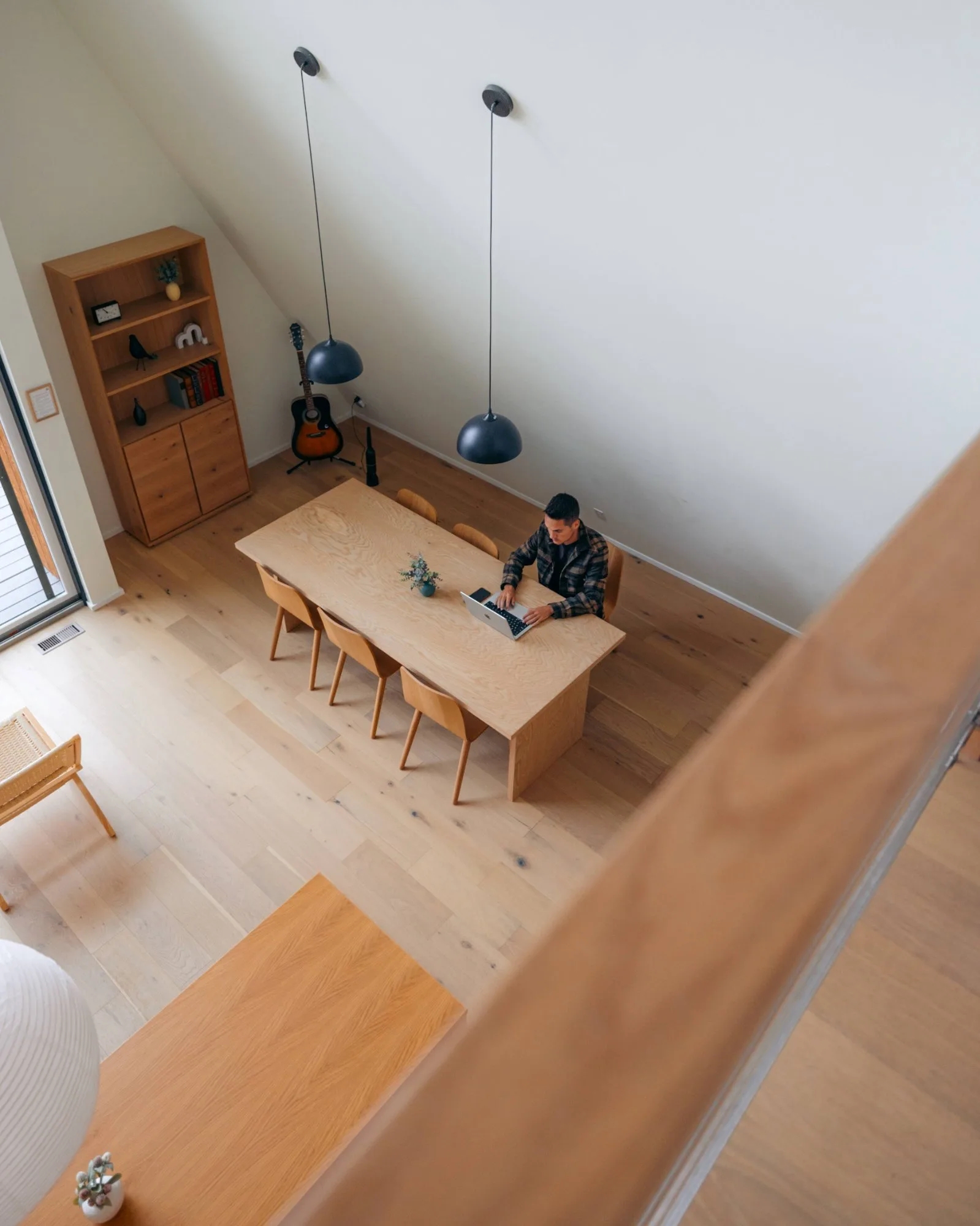 Overhead view of white-oak dining table with pendant lights and guitar at The A-Frame