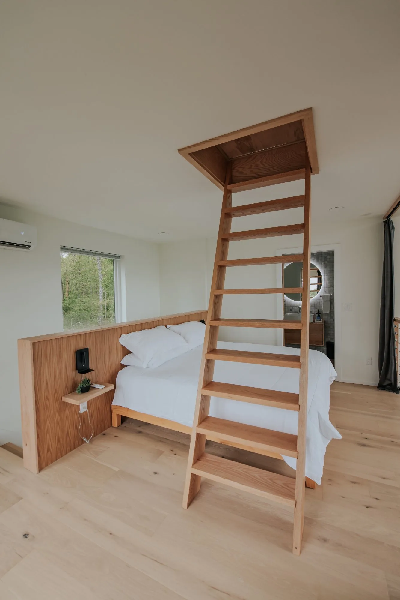 Primary bedroom with oak headboard and ship ladder to third-floor loft at The A-Frame